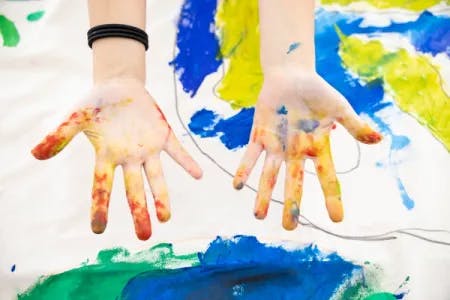 To håndflater med rød, gul og blå maling. Fotografi.